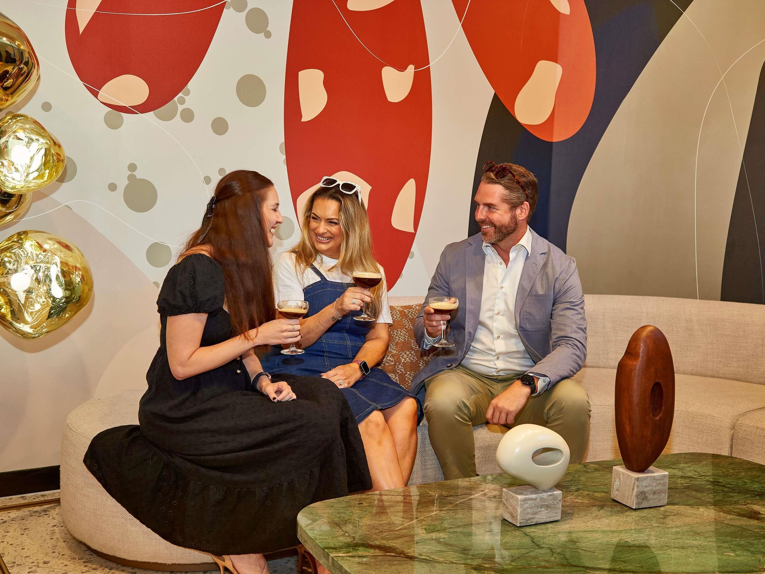 Un groupe de personnes est assis sur un canapé dans un intérieur moderne, agrémenté d’œuvres d’art abstraites sur les murs et d’une table basse en marbre.