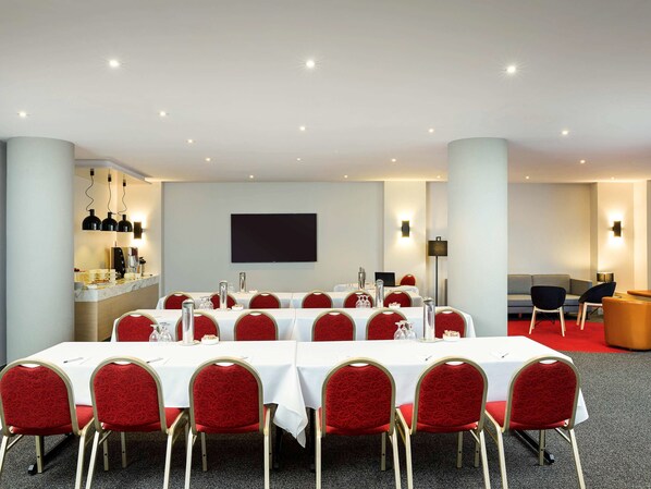 A conference room with a long table, red chairs, a bar area, and a flat-screen TV on the wall.