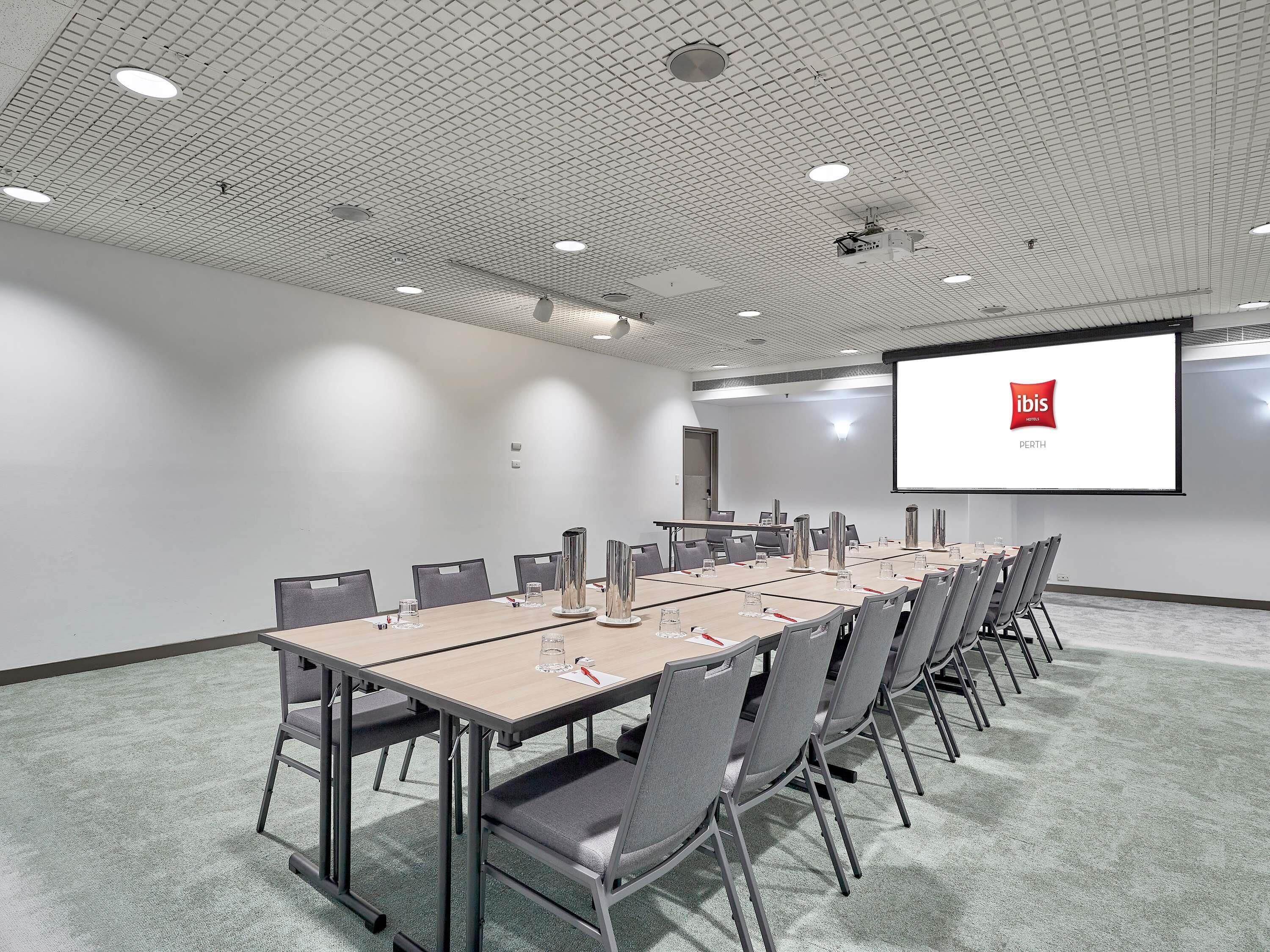A conference room with a long table, chairs, a projector screen, and a carpeted floor.