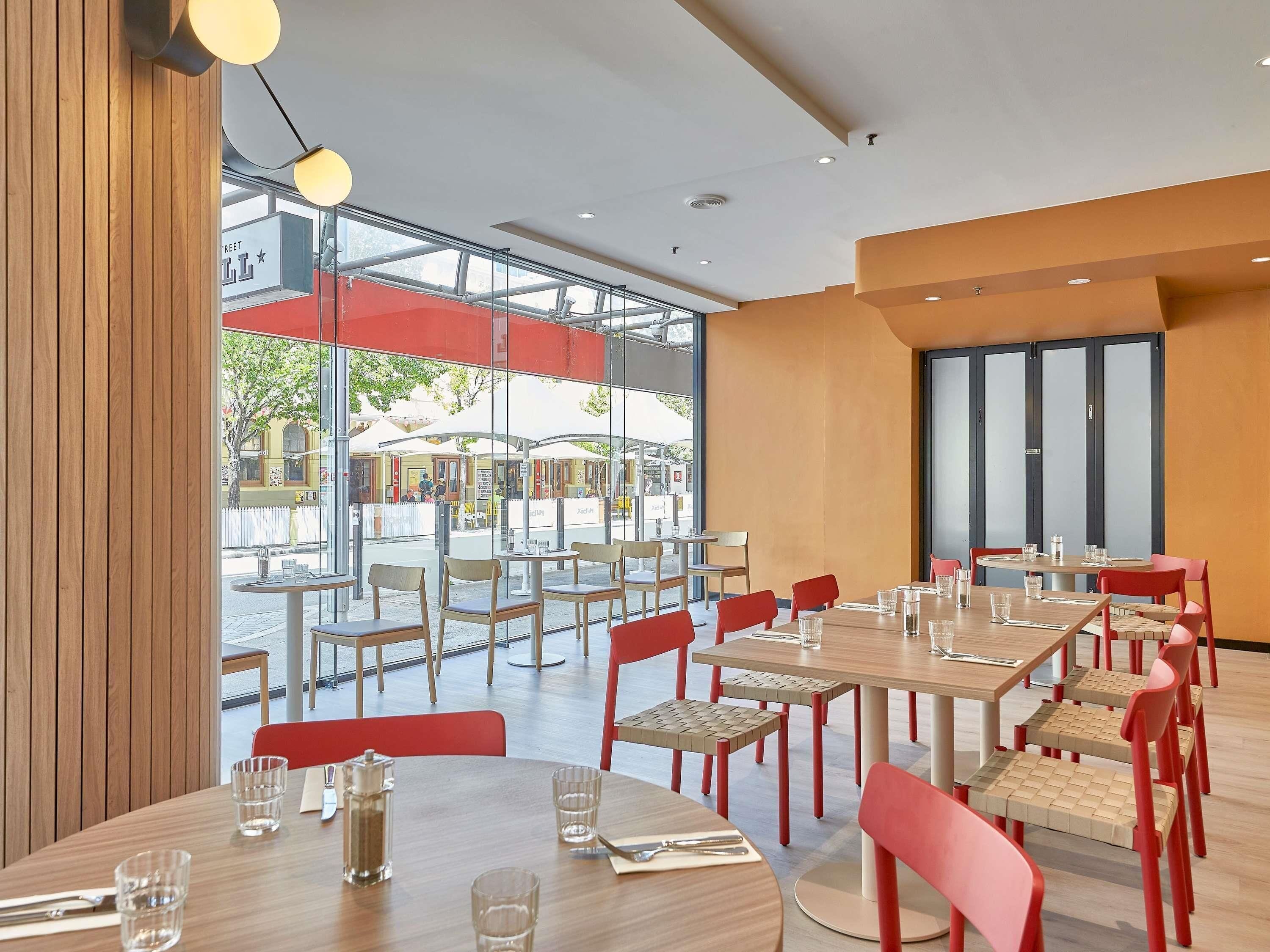 Un comedor interior con mesas y sillas, ventanas grandes y vistas a la calle.