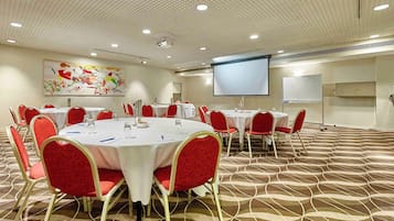 A conference room with round tables, red chairs, a projector screen, and a whiteboard.