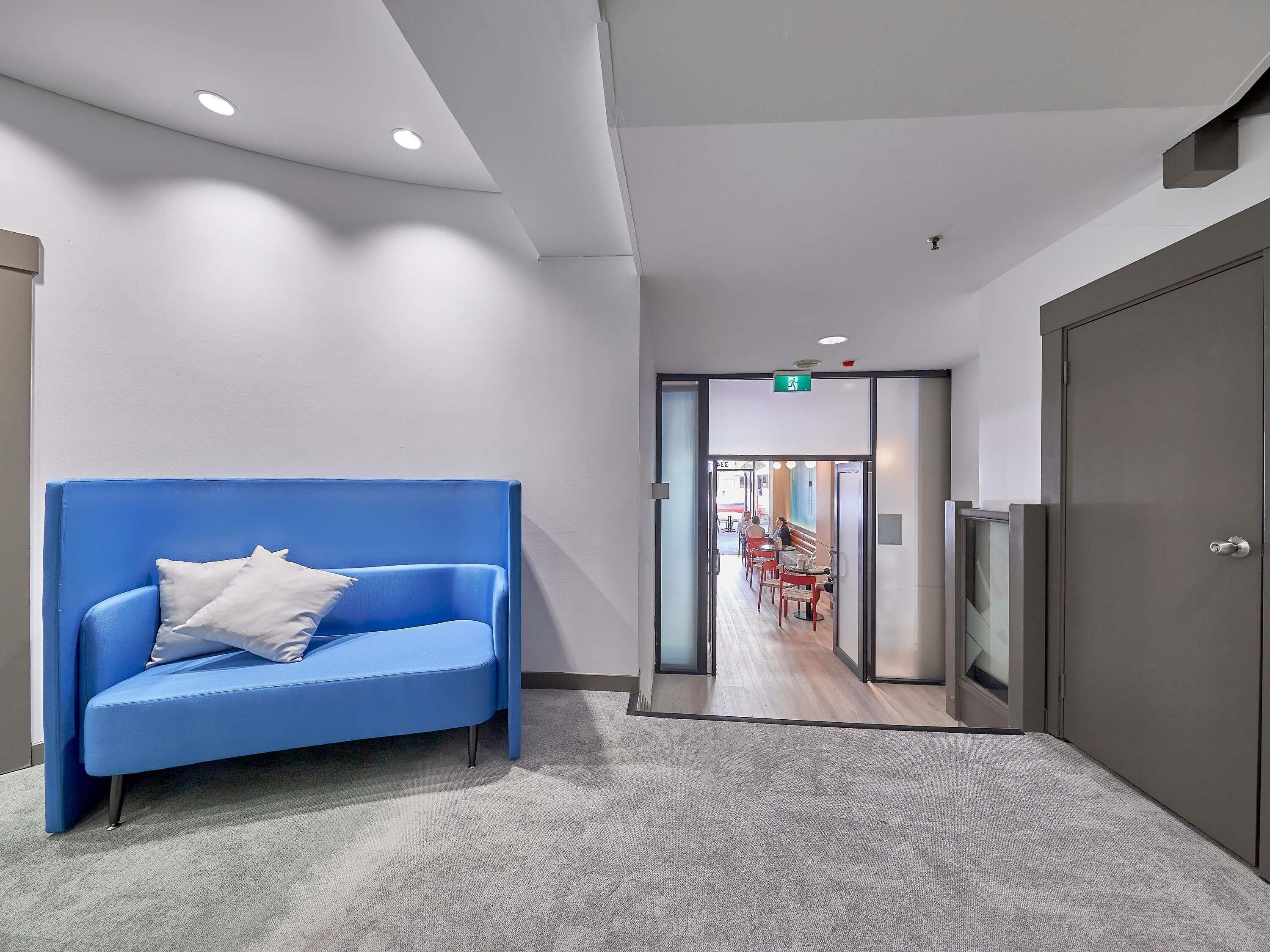 Un hall d’entrée moderne avec un canapé bleu, un sol recouvert de moquette et un couloir menant à un espace repas.