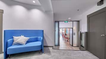 Un hall d’entrée moderne avec un canapé bleu, un sol recouvert de moquette et un couloir menant à un espace repas.