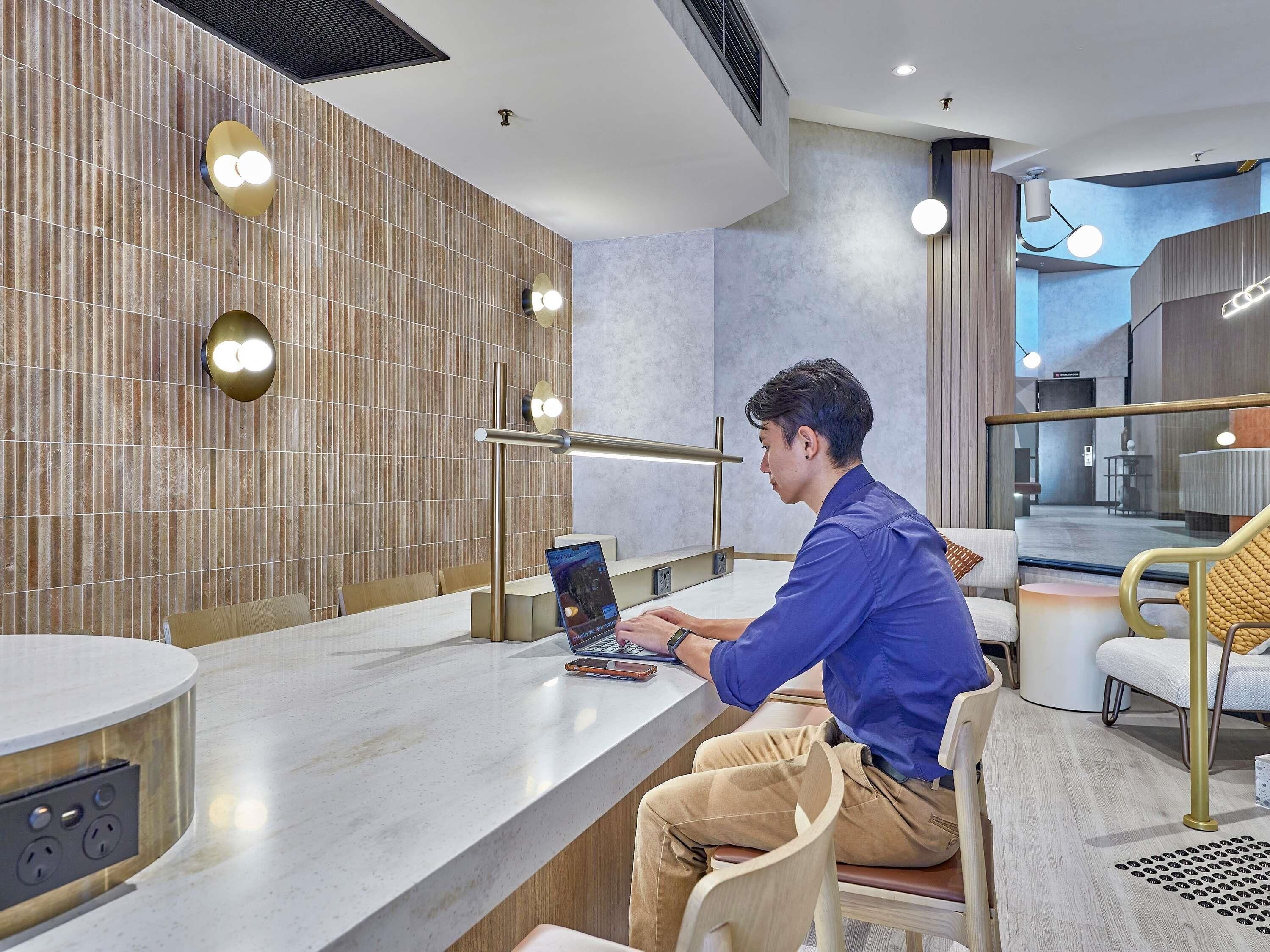 A modern hotel lobby with a seating area, a reception desk, and a large window offering a view of the interior.