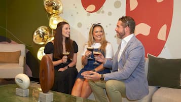 A group of people seated on a couch with a marble coffee table, a sofa, and a decorative wall with abstract patterns.