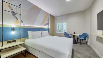 Habitación de hotel con cama, escritorio, dos sillas, televisor y ventana con vista a la ciudad.
