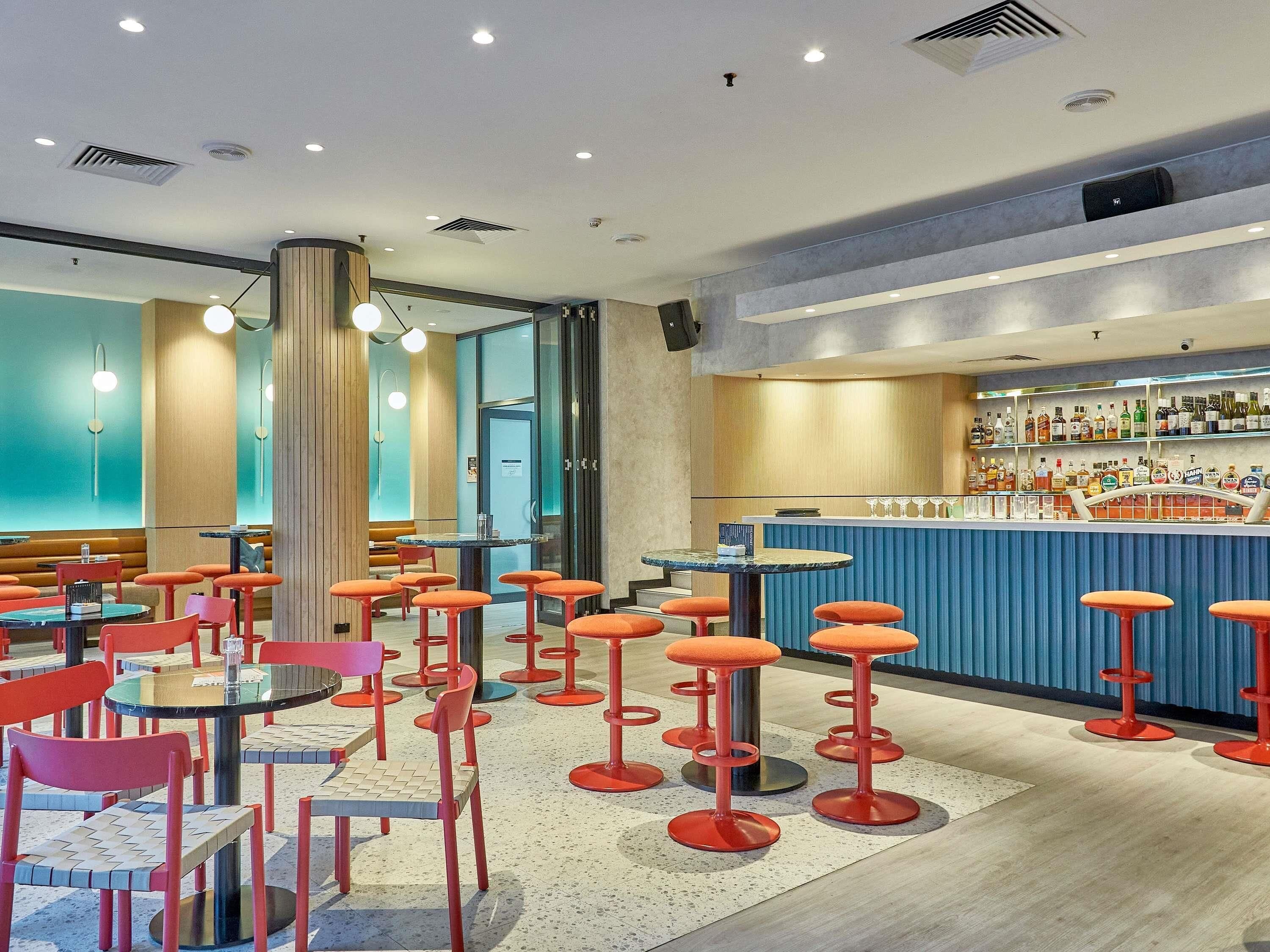 Zona de bar moderna con taburetes rojos, una barra azul y una variedad de botellas de licor.