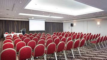 A conference room with rows of red chairs, a white table, a projector screen, and a large window.