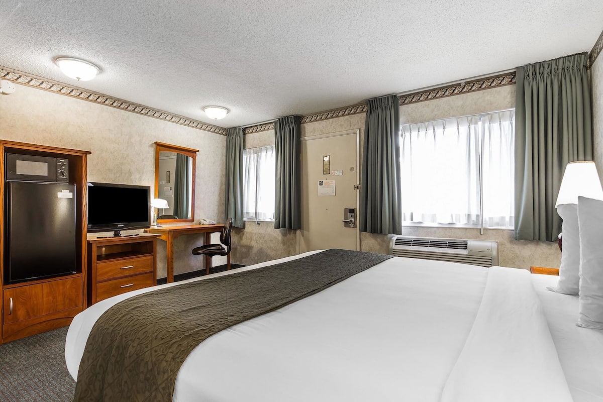 Ein Hotelzimmer mit Bett, Schreibtisch mit Fernseher, Kleiderschrank und Spiegel.