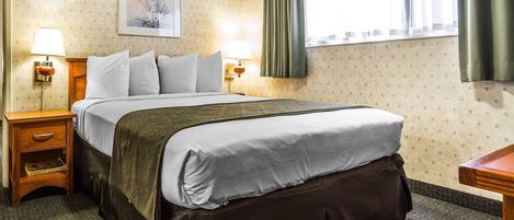 A hotel room with a large bed, two bedside tables with lamps, a framed picture on the wall, and a window with curtains.