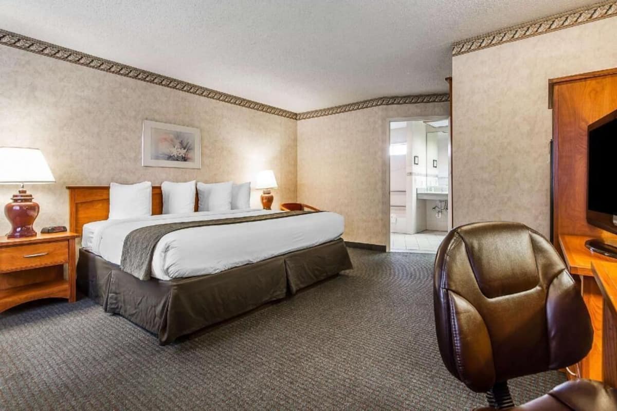 Ein Hotelzimmer mit Bett, Nachttischen, einem Sessel, einem Fernseher und einer Tür zu einem Badezimmer.