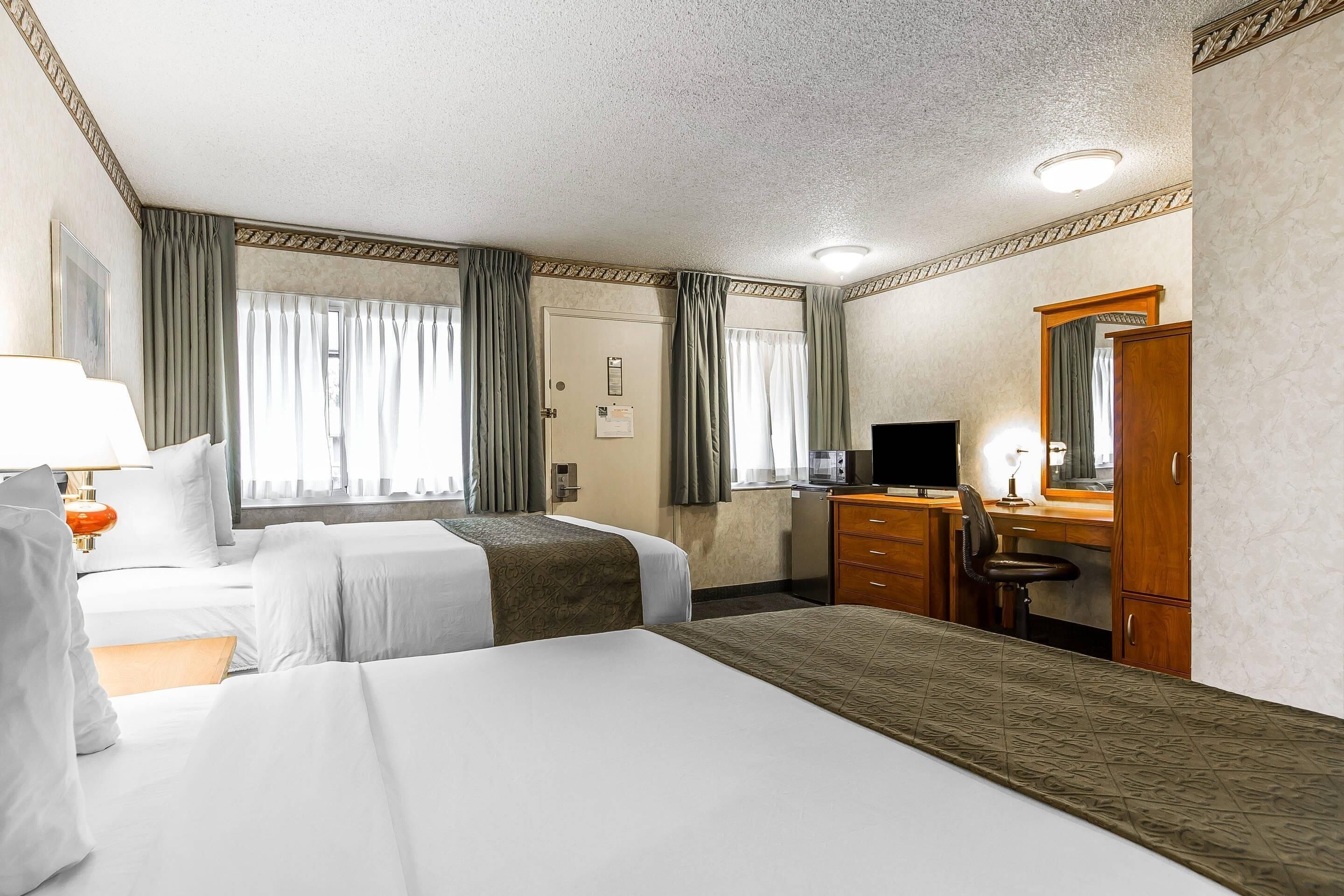 A hotel room with two beds, a desk, a chair, a television, and a wardrobe.