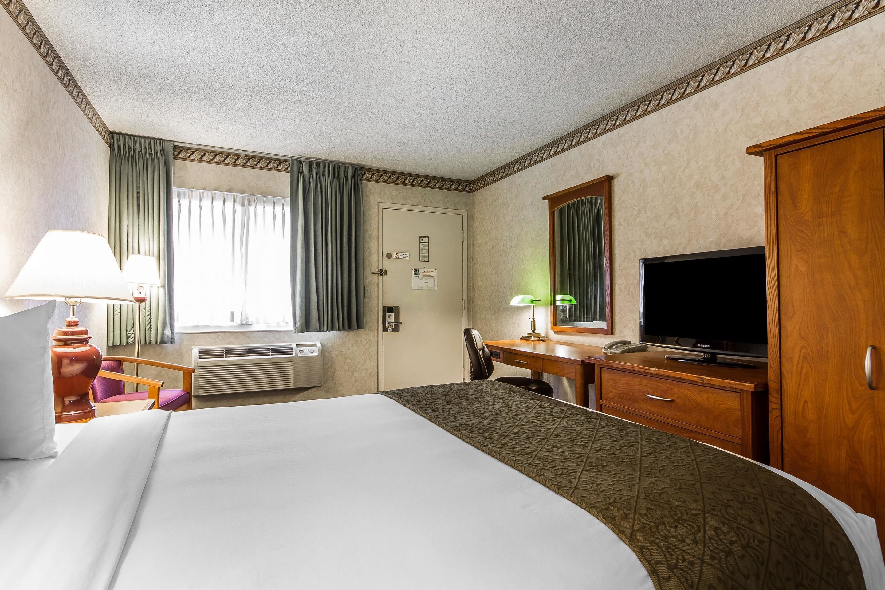 Una camera d'albergo con un letto grande, una scrivania con televisore, una sedia, una lampada e una finestra con tende.