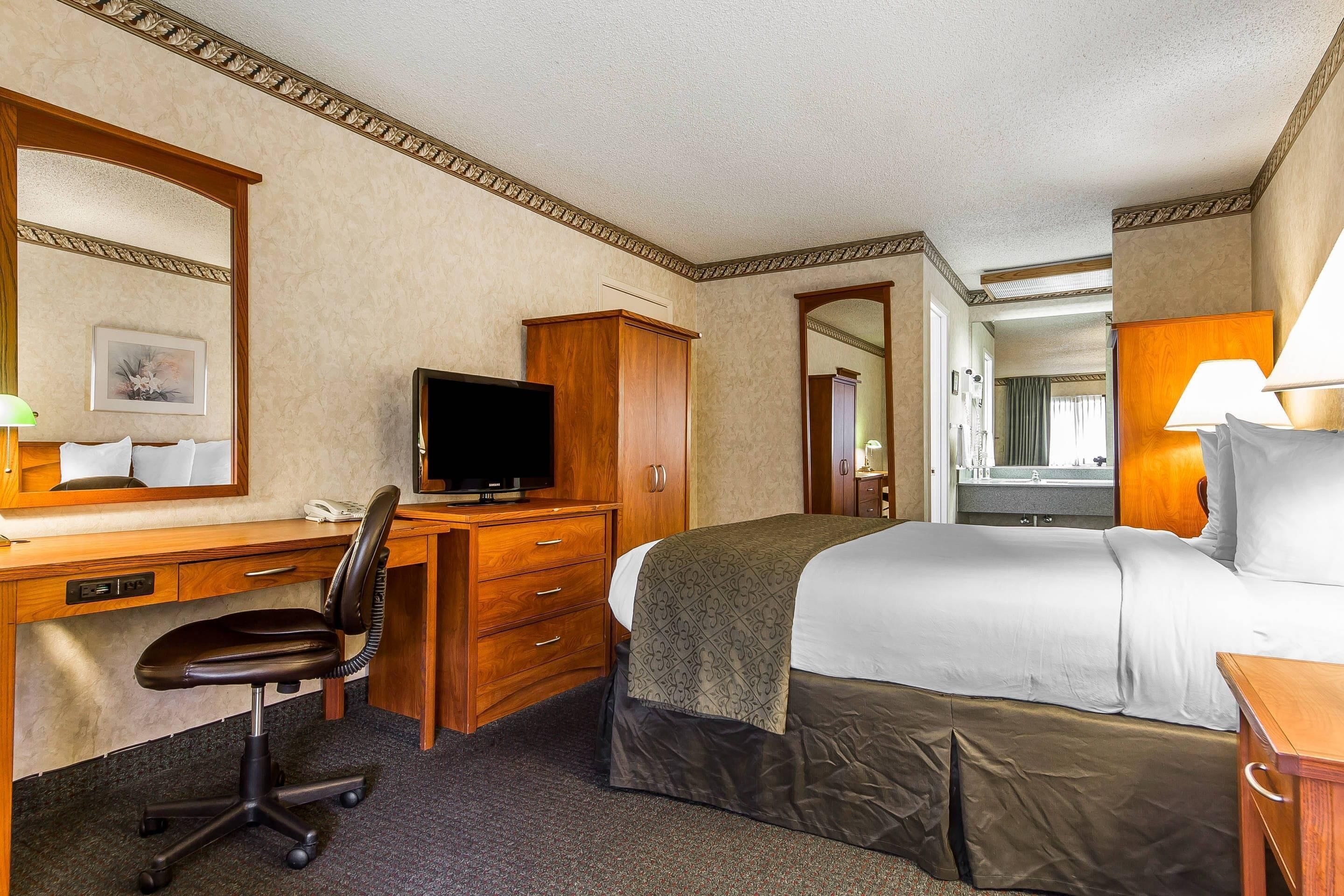 A hotel room with a bed, desk, chair, television, and a mirror.
