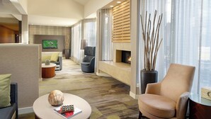 A modern hotel room with a cozy seating area, a flat-screen TV, a fireplace, and a large window with sheer curtains.