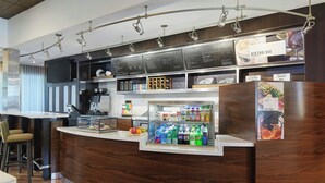 A modern bar area with a wooden counter, a beverage dispenser, and a menu board.