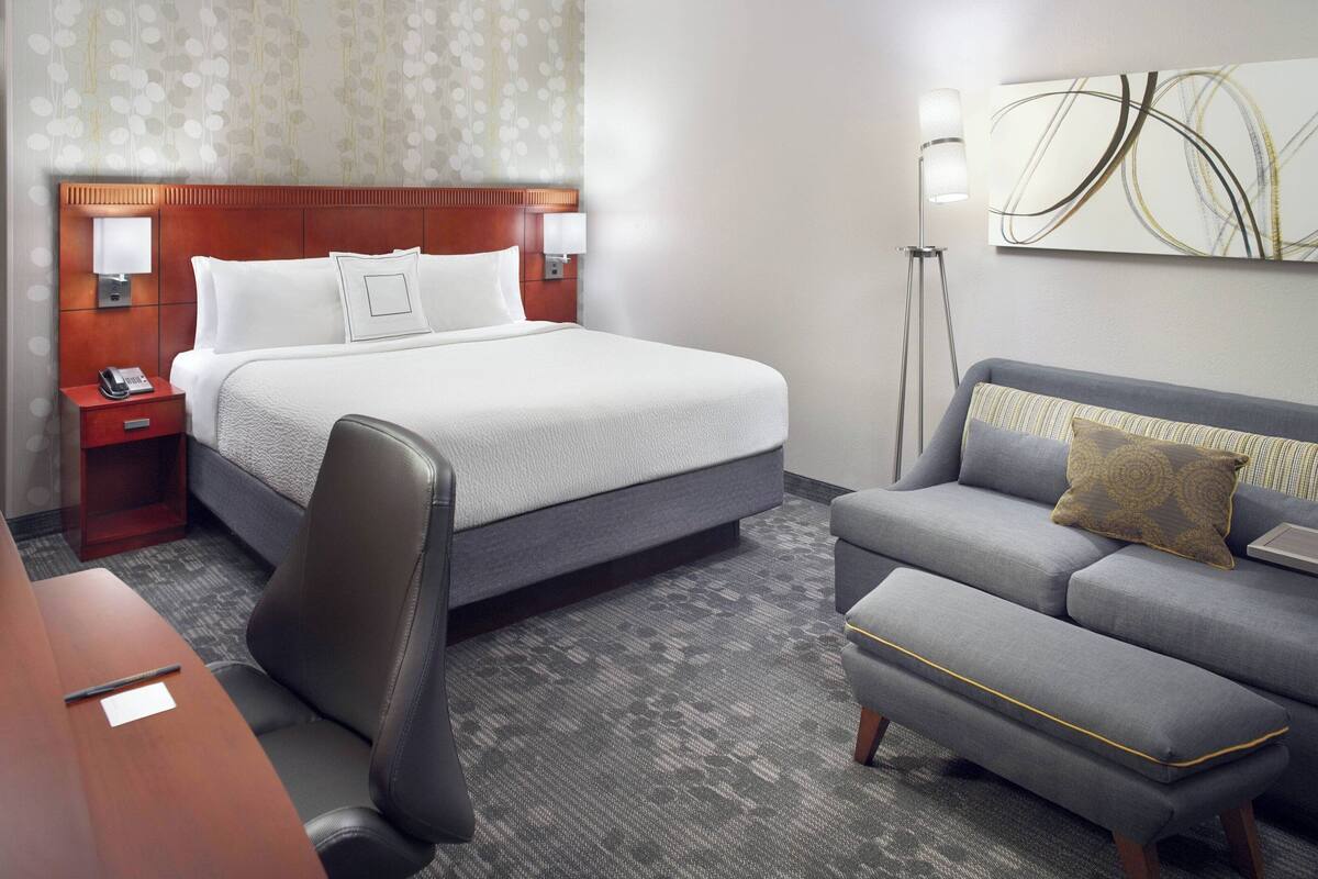 A hotel room with a large bed, a desk with a chair, a sofa, and a standing lamp.