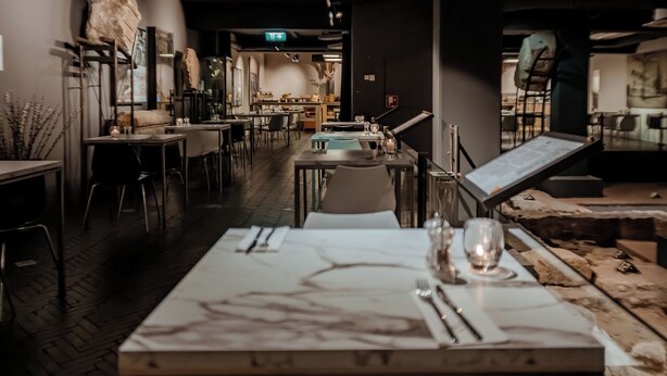A restaurant with a long table set for dining, chairs, and a menu stand. - Derlon Hotel Maastricht (Maastricht)