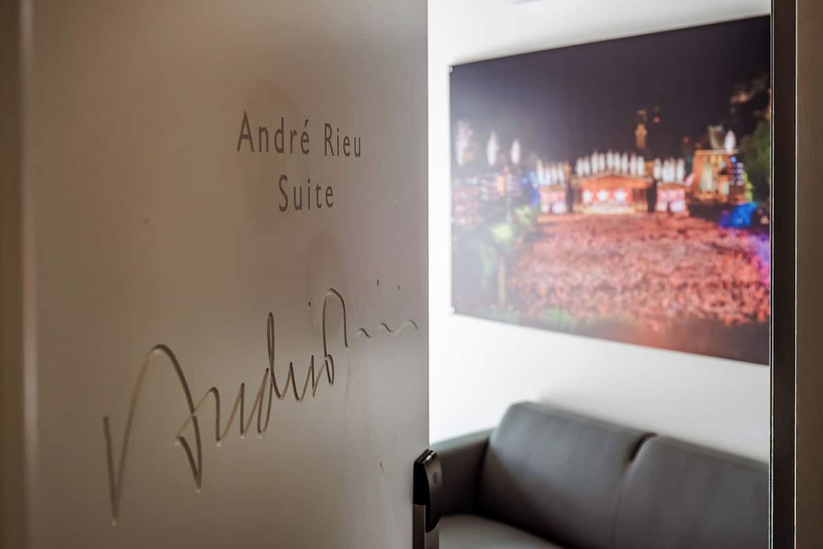 Eine Wand mit der Aufschrift 'André Rieu Suite' und einer Unterschrift, ein Sofa und ein großes gerahmtes Bild eines Gebäudes bei Nacht.