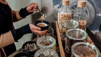 Une personne sert des céréales d’un bol dans une tasse, et divers aliments sont disposés dans des bocaux en verre sur un plateau en bois.