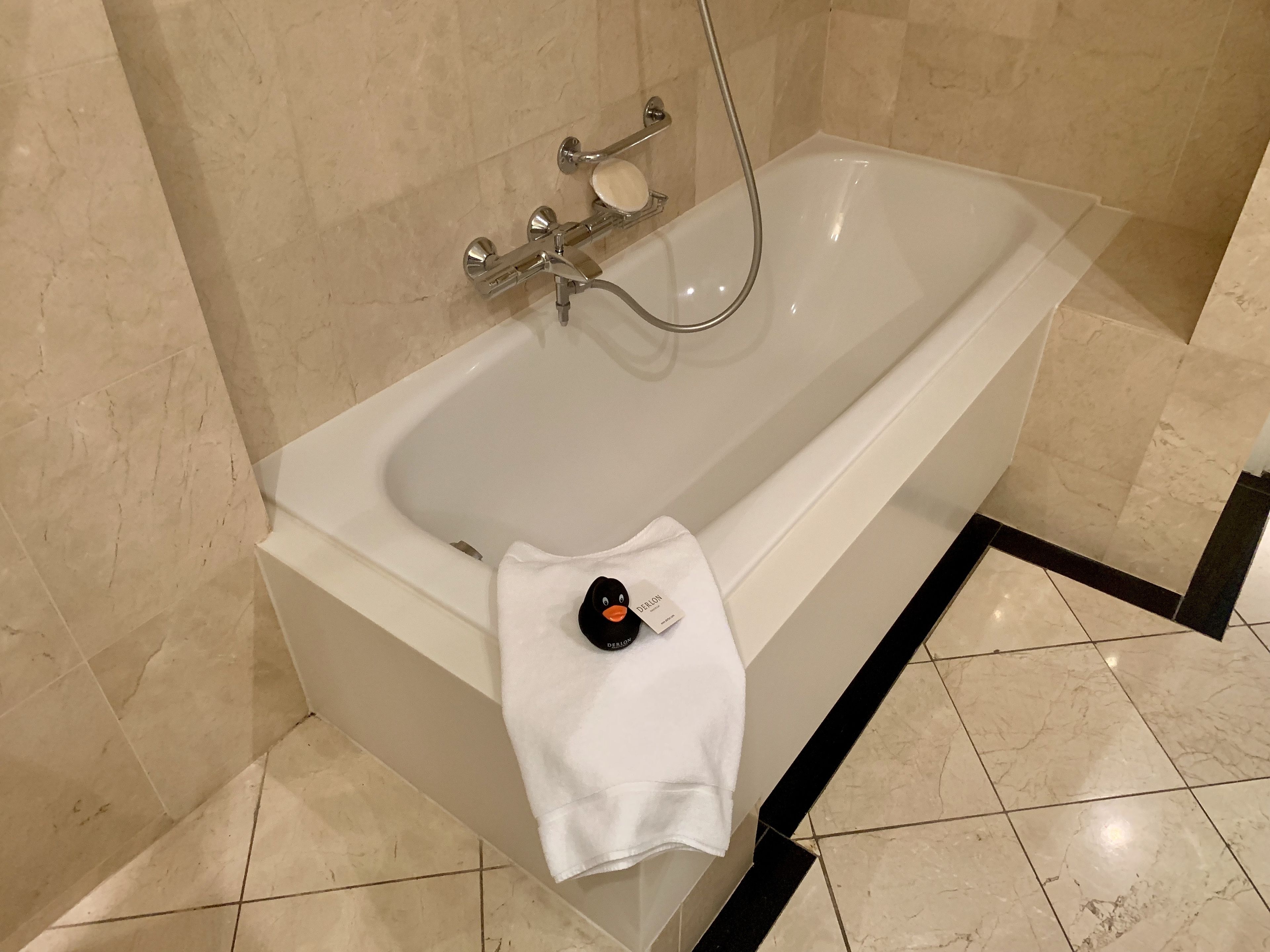 A modern bathroom with a white bathtub, a handheld showerhead, and a white towel with a duck-shaped bath mat.