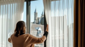 A person adjusting curtains in a room with a view of a building with towers. - Derlon Hotel Maastricht (Maastricht)