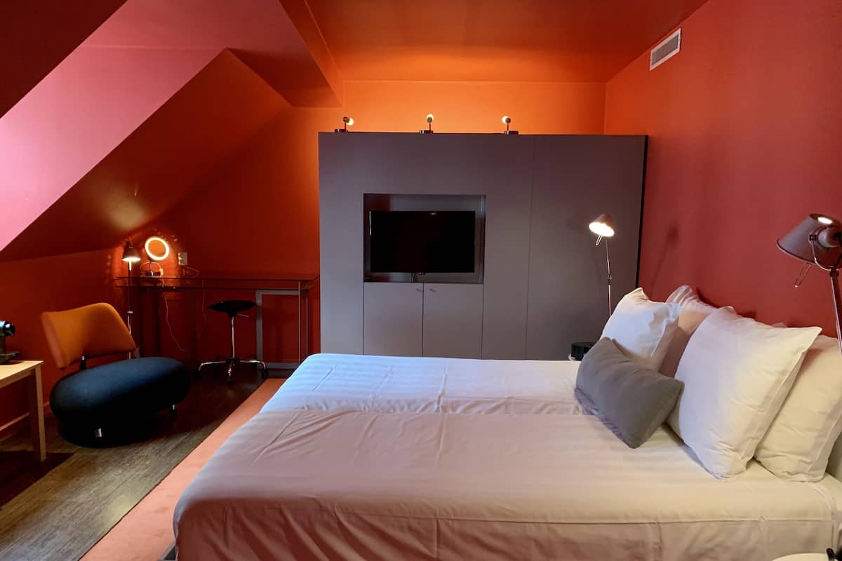 Ein Schlafzimmer mit einem großen Bett, einem Schreibtisch mit Stuhl, einem an der Wand befestigten Fernseher und einer Lampe.