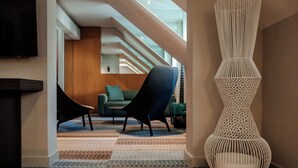 A modern interior with a staircase, a black chair, a white decorative vase, and a flat-screen TV. - Derlon Hotel Maastricht (Maastricht)