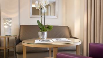 A modern hotel room with a round glass table, a leather sofa, a purple chair, and a potted orchid.