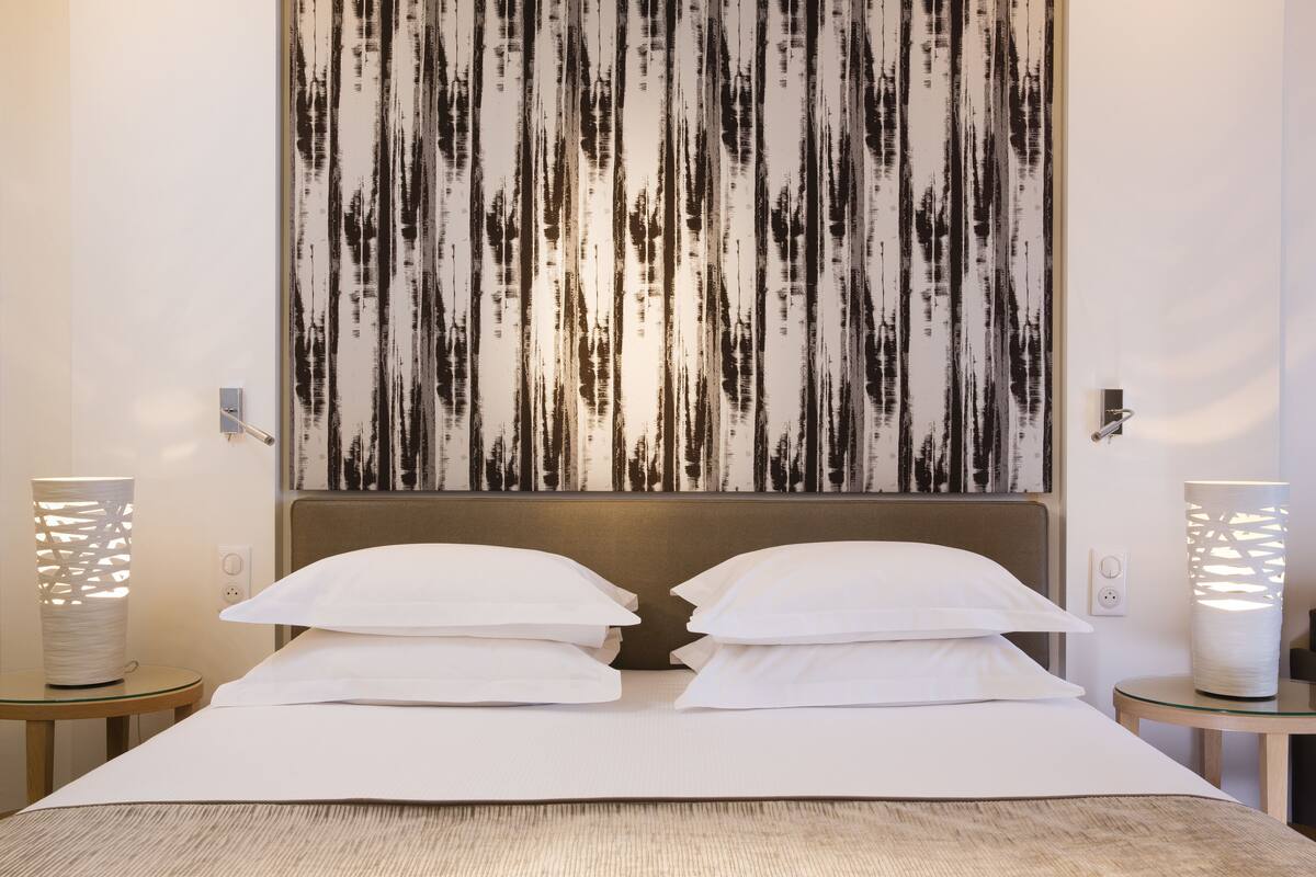 A hotel room with a large bed, two bedside tables, a wall-mounted artwork, and a modern lamp.
