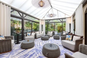 A sunroom with wicker furniture, a patterned rug, and large windows overlooking a garden.