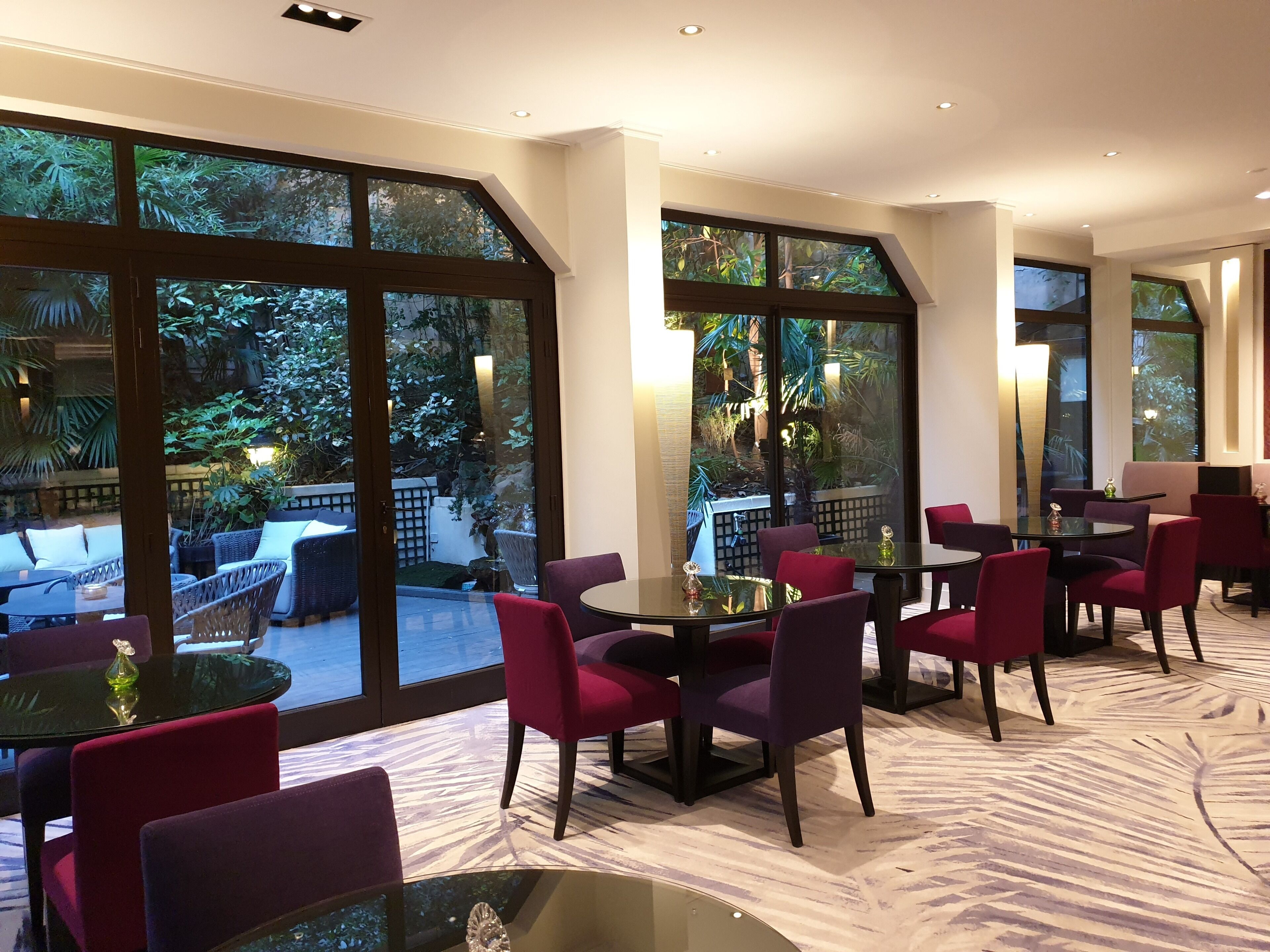 Un espace repas moderne avec de grandes fenêtres, des meubles en osier et des chaises rouges.