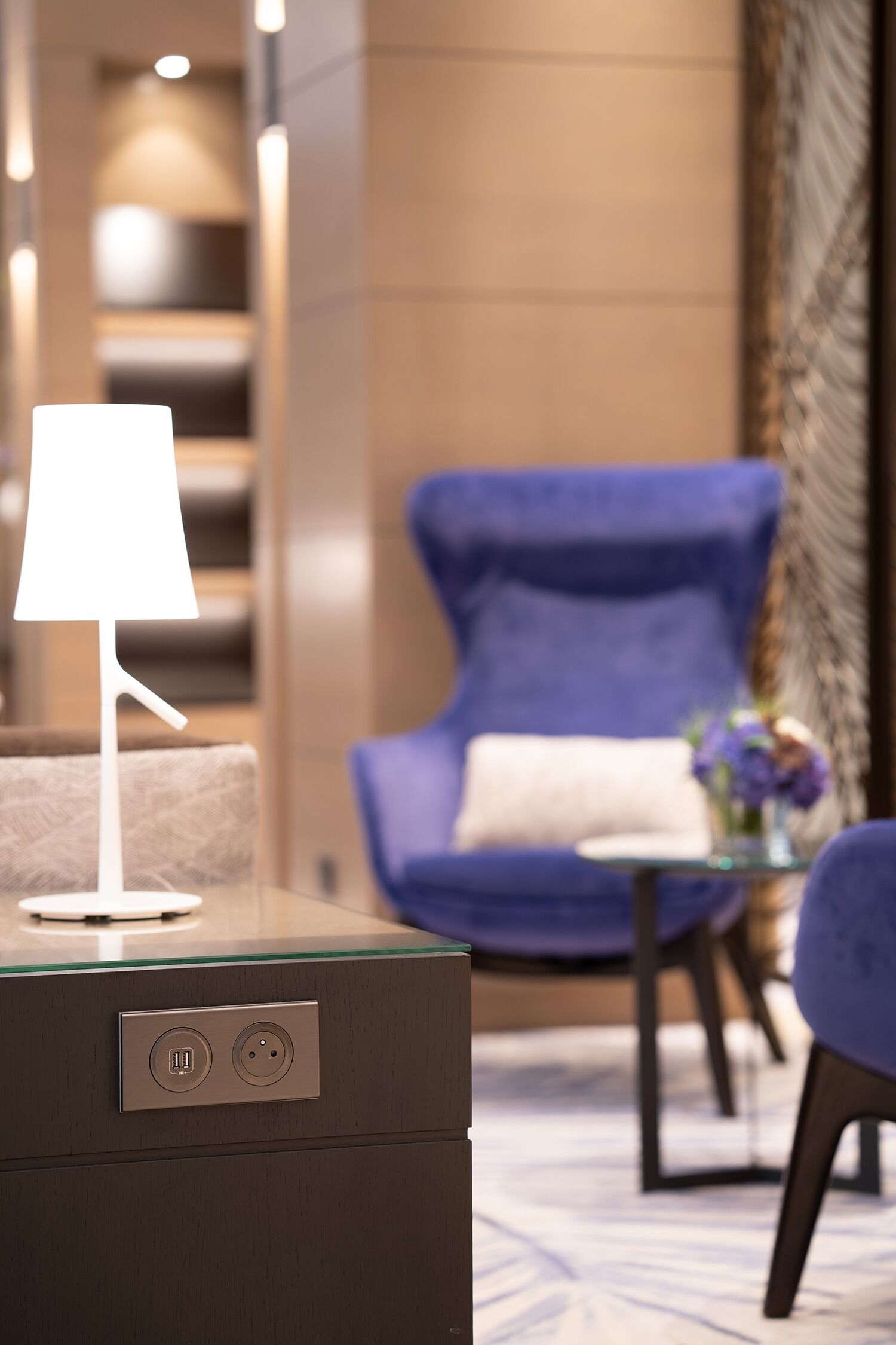 Una habitación moderna con una mesa de vidrio, una silla azul y una lámpara.