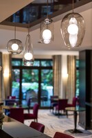 A modern interior with hanging pendant lights, a dining area with red chairs, and large windows offering a view of greenery outside.