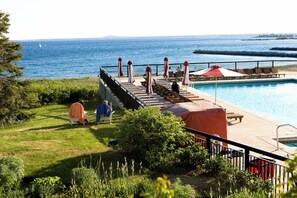 A poolside area with a view of the sea, a covered deck, and lounge chairs.
