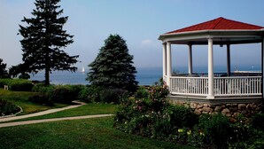 A gazebo with a red roof, surrounded by a garden with various plants and flowers, near a body of water. - The Colony Hotel (Kennebunkport)