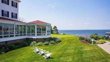 A coastal property with a covered patio, a lawn with lawn chairs, and a view of the sea.