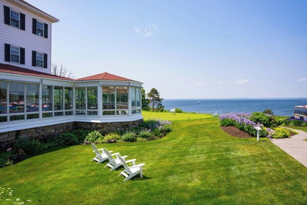 A coastal property with a covered patio, a lawn with lawn chairs, and a view of the sea.