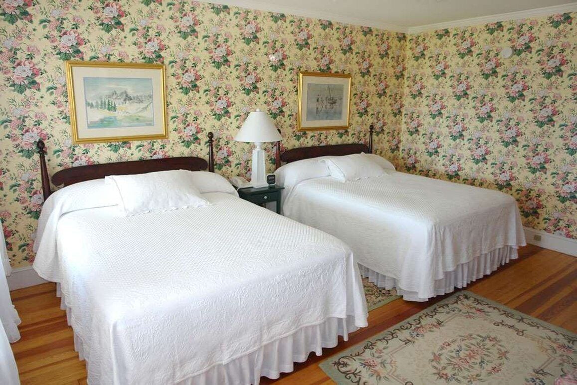Una habitación con dos camas, papel tapiz floral y dos cuadros en la pared.