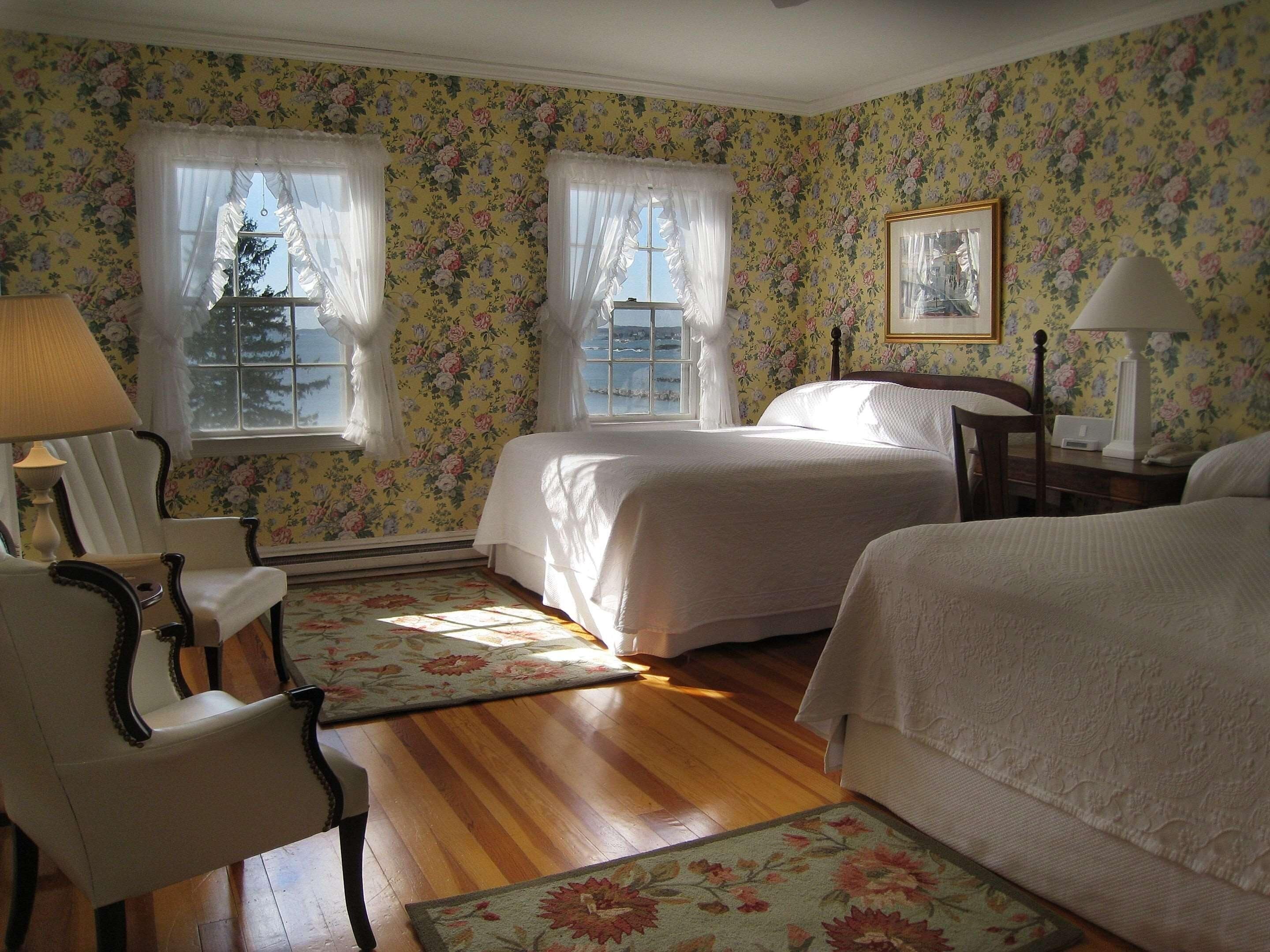 A room with two beds, a chair, a desk, and a window with curtains.