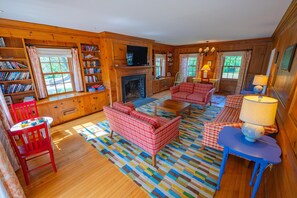 A cozy living room with a fireplace, wooden bookshelves, and a colorful rug. - The Colony Hotel (Kennebunkport)