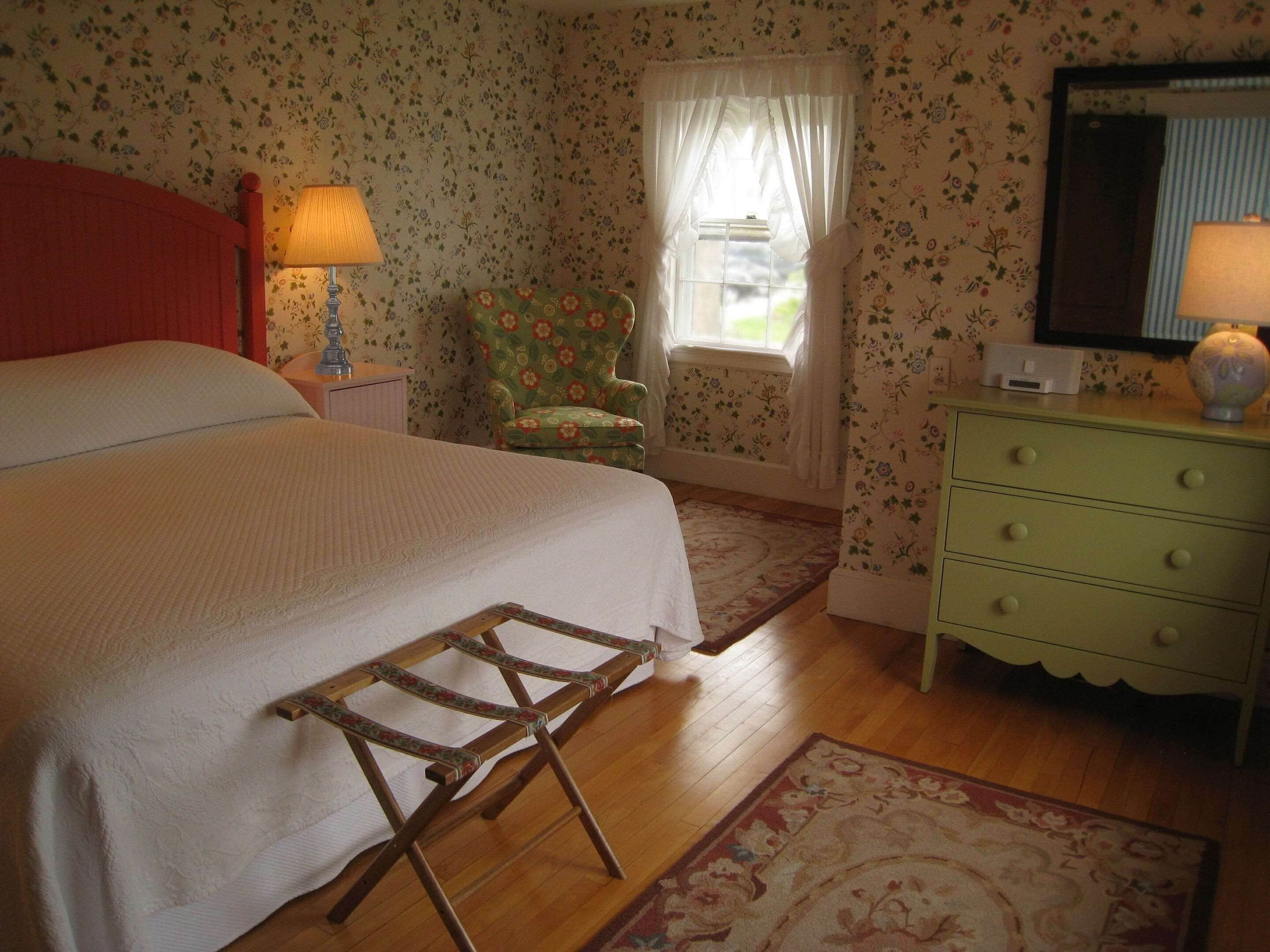A bedroom with a bed, a chair, a dresser, and a window with curtains.