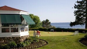 Un bâtiment doté d’un auvent vert, de fondations en pierre et offrant une vue sur un terrain de golf avec des drapeaux.