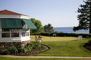 A building with a green awning, a stone foundation, and a view of a golf course with flags.