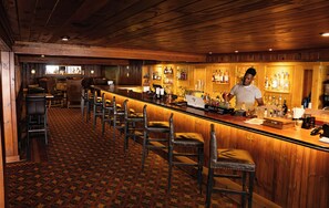 A bar area with wooden bar counters, leather bar stools, and a patterned carpet. - The Colony Hotel (Kennebunkport)