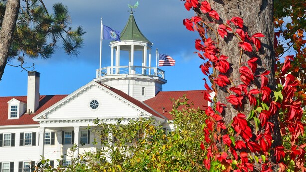 A white building with a green roof, a tower with a flag, and red foliage. - The Colony Hotel (Kennebunkport)