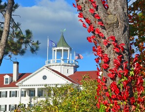 A white building with a green roof, a tower with a flag, and red foliage. - The Colony Hotel (Kennebunkport)