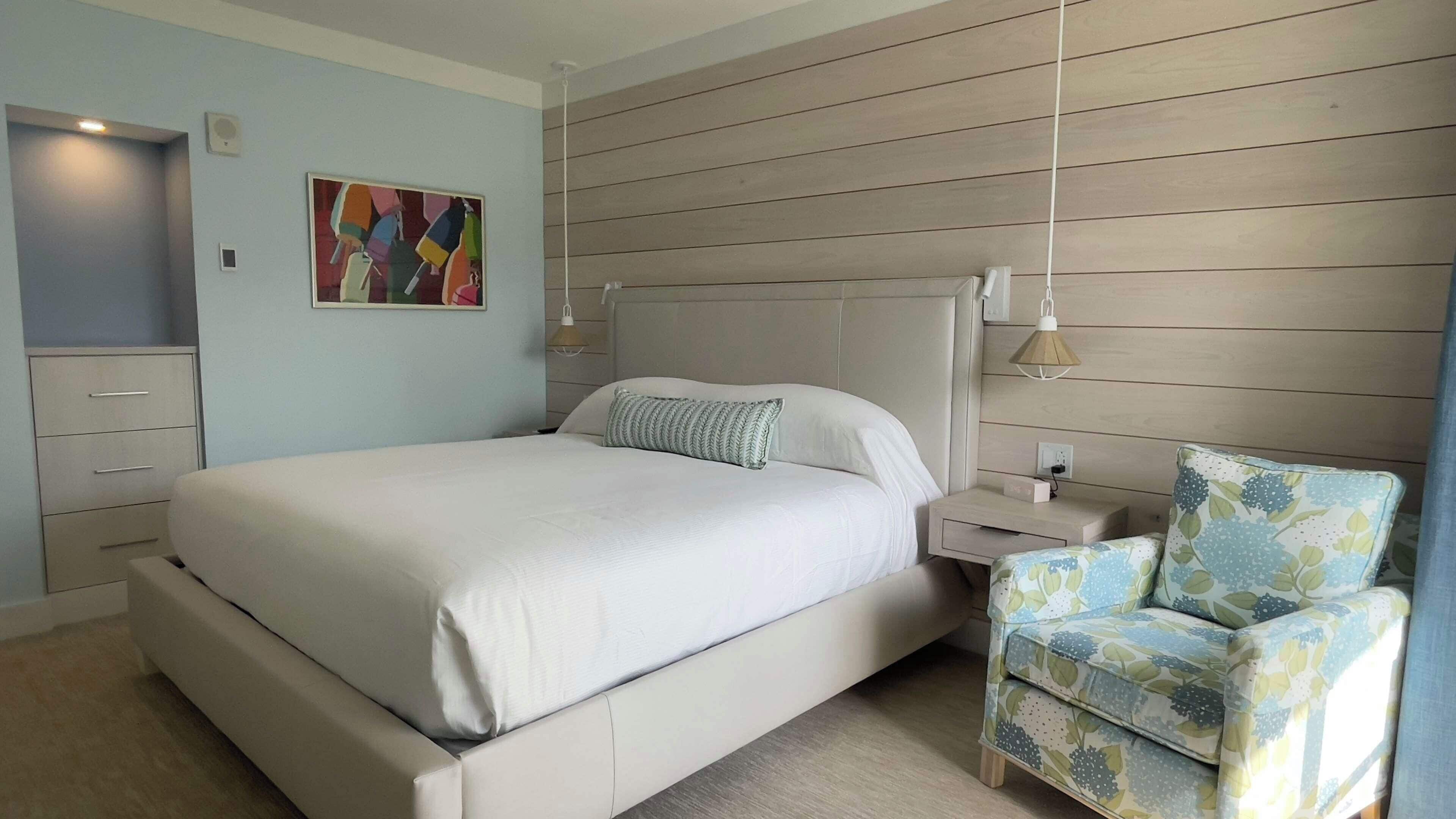 A bedroom with a bed, bedside tables, a chair, and a wall-mounted artwork.