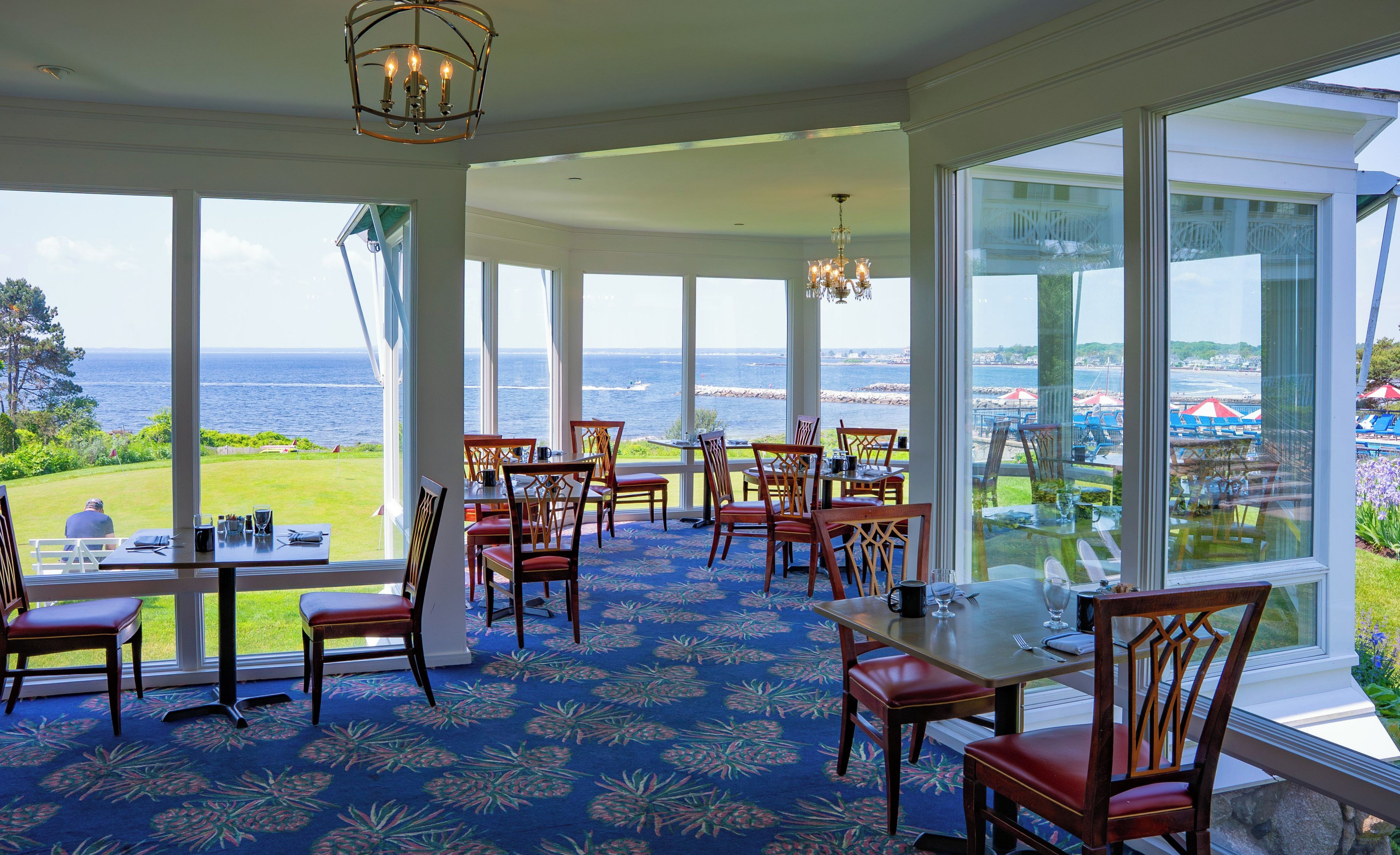 A dining area with large windows overlooking a scenic view of the sea and a beach.