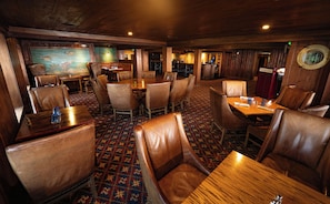 A restaurant with wooden walls, leather chairs, and a patterned carpet. Tables are set with glasses and cutlery.